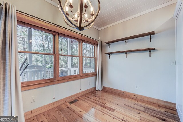 spare room with light hardwood / wood-style floors, a healthy amount of sunlight, an inviting chandelier, and crown molding