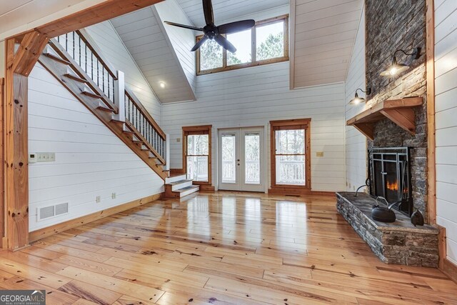 unfurnished living room with wood walls, high vaulted ceiling, light wood-type flooring, a fireplace, and ceiling fan