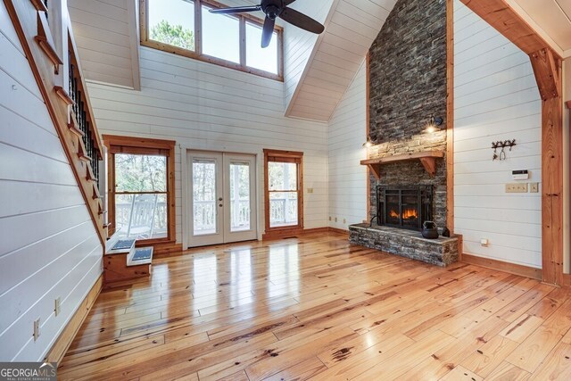 unfurnished living room with ceiling fan, high vaulted ceiling, wood walls, and light hardwood / wood-style floors