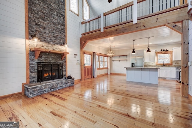 living room with sink, a fireplace, a towering ceiling, ornamental molding, and light hardwood / wood-style flooring