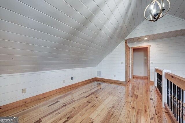 bonus room featuring vaulted ceiling, light hardwood / wood-style floors, and wooden walls