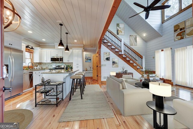 living room featuring wooden walls, wood ceiling, light wood-type flooring, ceiling fan, and sink