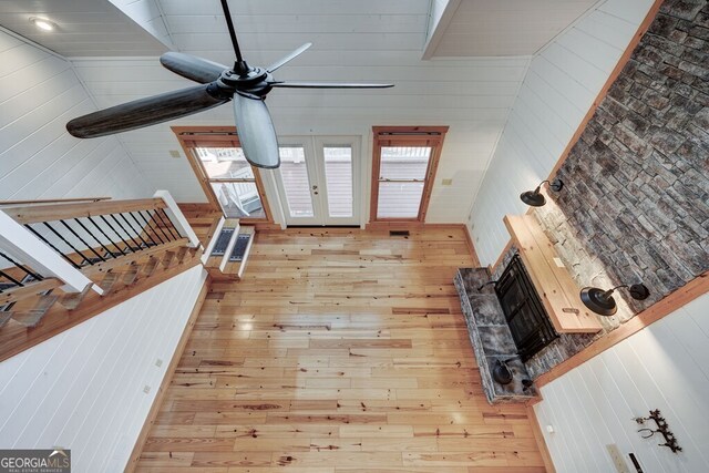 living room with french doors, wooden walls, high vaulted ceiling, and light hardwood / wood-style floors