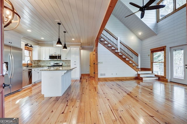 kitchen with light stone countertops, hanging light fixtures, stainless steel appliances, a kitchen island, and white cabinets