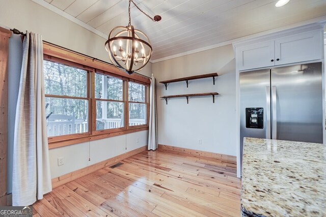 interior space with white cabinets, light stone counters, light wood-type flooring, pendant lighting, and a notable chandelier