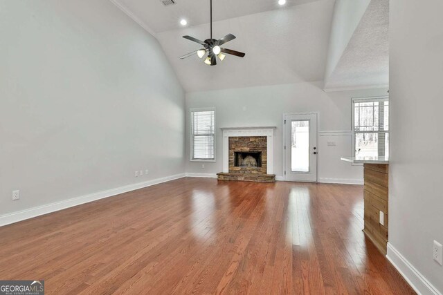 unfurnished living room featuring a textured ceiling, vaulted ceiling, ceiling fan, wood-type flooring, and a stone fireplace