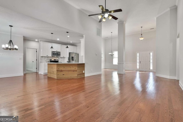 unfurnished living room with ceiling fan with notable chandelier, a towering ceiling, ornamental molding, and light hardwood / wood-style flooring