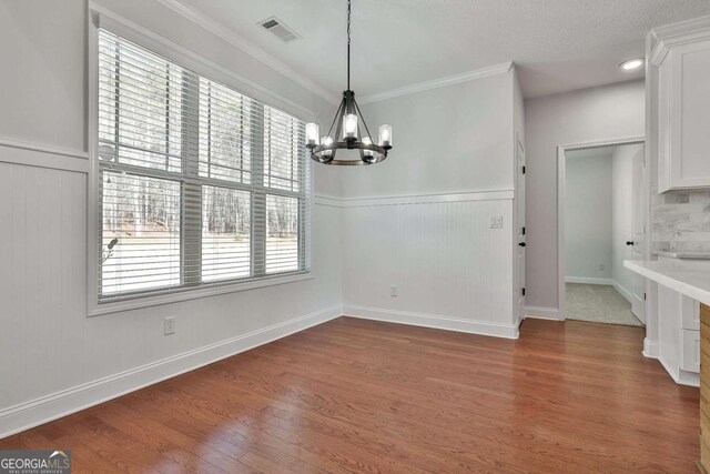 unfurnished dining area featuring a textured ceiling, dark hardwood / wood-style flooring, an inviting chandelier, and crown molding