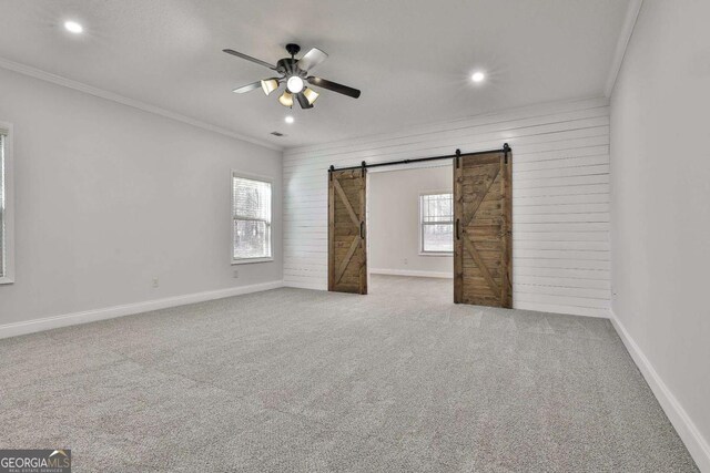 interior space featuring a barn door, carpet, ceiling fan, wooden walls, and multiple windows