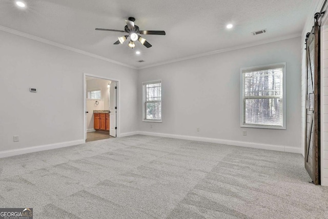 unfurnished bedroom featuring ceiling fan, light colored carpet, connected bathroom, and a barn door