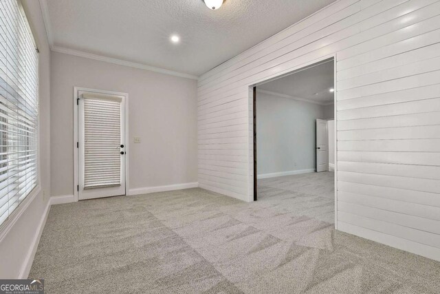 carpeted spare room featuring a textured ceiling, ornamental molding, and wood walls