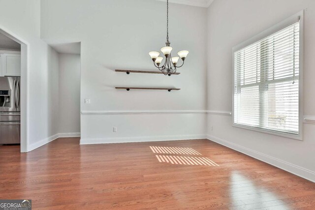 unfurnished dining area featuring ornamental molding, a notable chandelier, a wealth of natural light, and hardwood / wood-style floors