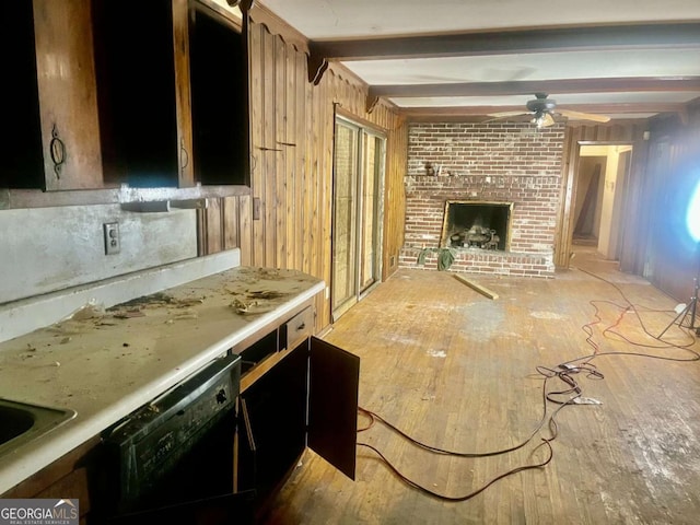 unfurnished living room featuring beamed ceiling, ceiling fan, a brick fireplace, wooden walls, and light hardwood / wood-style flooring