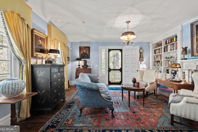 living area with crown molding, built in shelves, a notable chandelier, and dark wood-type flooring