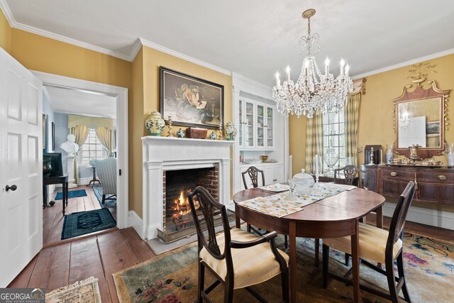 dining space with a brick fireplace, crown molding, a chandelier, and hardwood / wood-style floors