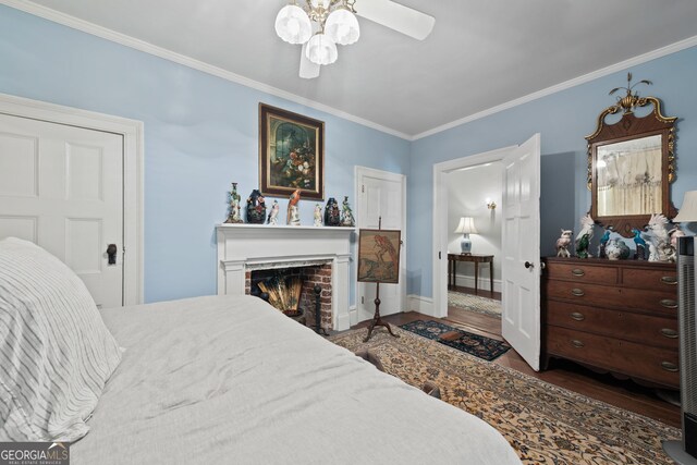 bedroom with ceiling fan, a brick fireplace, crown molding, and wood-type flooring