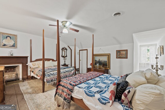 bedroom featuring vaulted ceiling, a fireplace, ceiling fan, and wood-type flooring