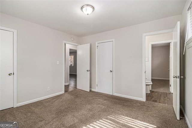 unfurnished bedroom featuring ensuite bathroom and dark carpet