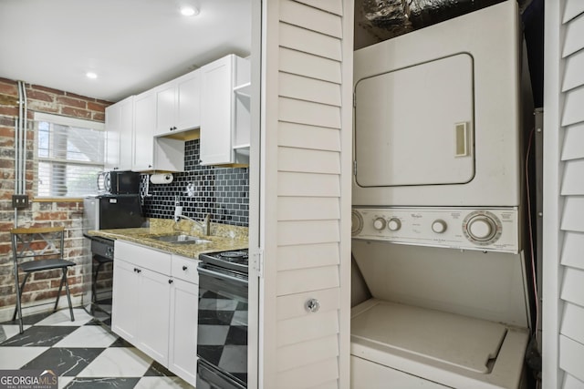 kitchen with brick wall, white cabinets, electric range, and stacked washer and clothes dryer