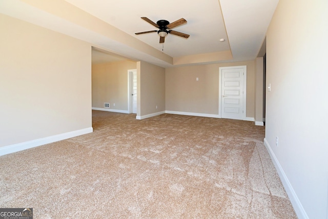 spare room featuring a ceiling fan, a raised ceiling, light carpet, and baseboards