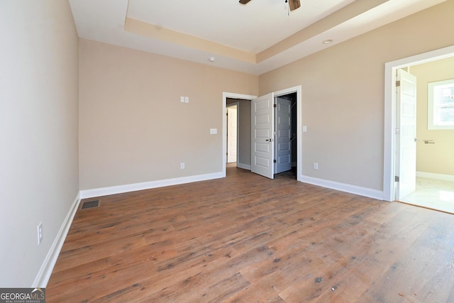 unfurnished bedroom with a raised ceiling, visible vents, baseboards, and hardwood / wood-style floors