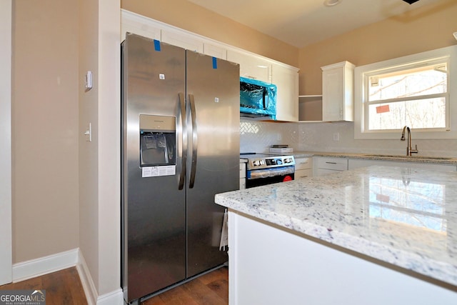 kitchen with dark wood-style floors, appliances with stainless steel finishes, white cabinetry, a sink, and light stone countertops