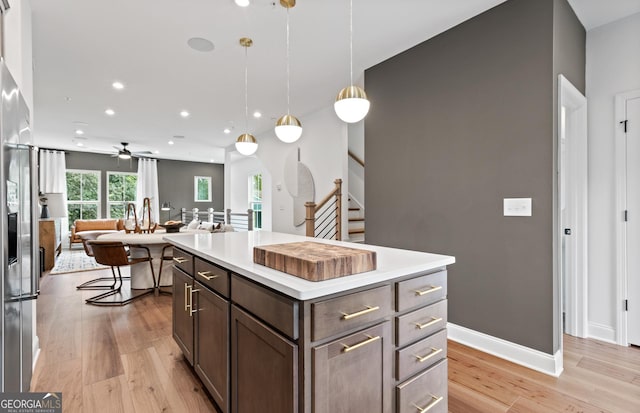 kitchen featuring ceiling fan, pendant lighting, a kitchen island, light hardwood / wood-style flooring, and dark brown cabinets