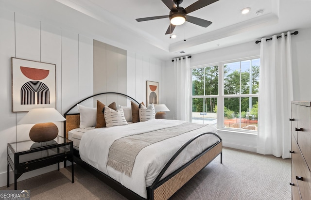 carpeted bedroom with a raised ceiling and ceiling fan