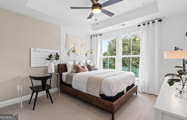 bedroom with a raised ceiling, ceiling fan, and light colored carpet