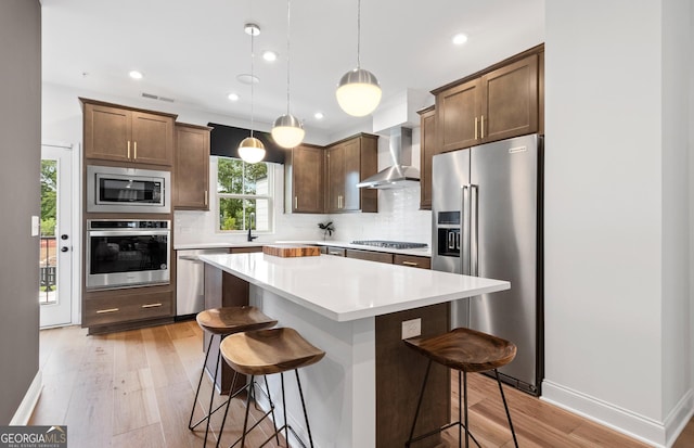 kitchen featuring stainless steel appliances, wall chimney range hood, a kitchen bar, and a center island