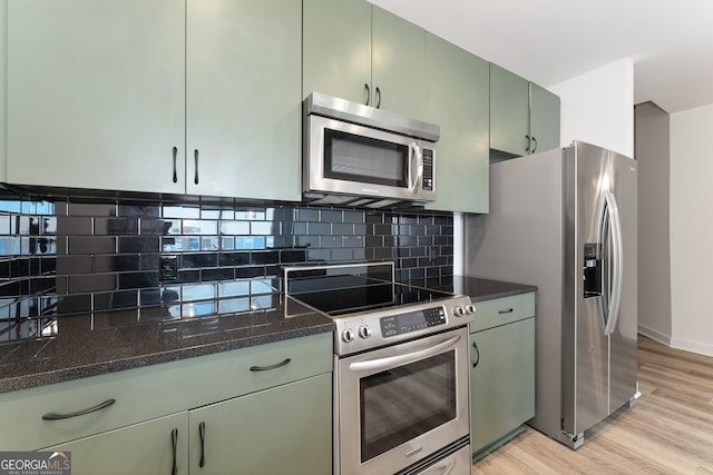 kitchen with stainless steel appliances, green cabinetry, light hardwood / wood-style floors, backsplash, and dark stone counters