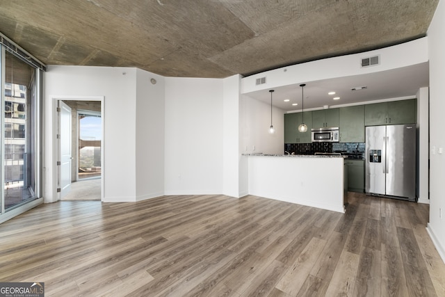 kitchen with kitchen peninsula, hardwood / wood-style flooring, hanging light fixtures, tasteful backsplash, and appliances with stainless steel finishes