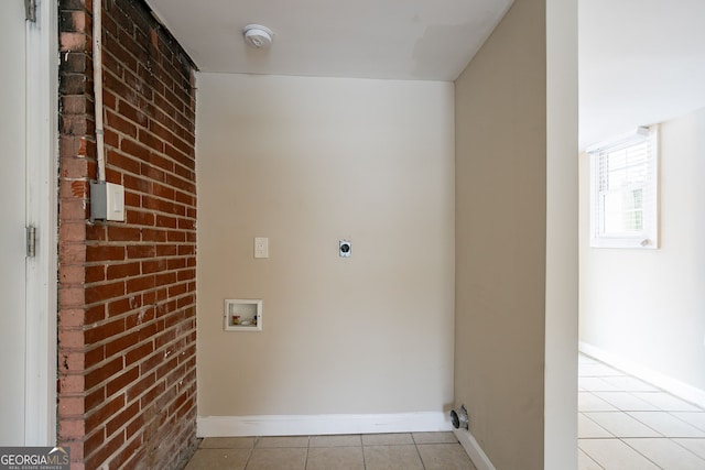 laundry area with electric dryer hookup, washer hookup, light tile patterned floors, and brick wall