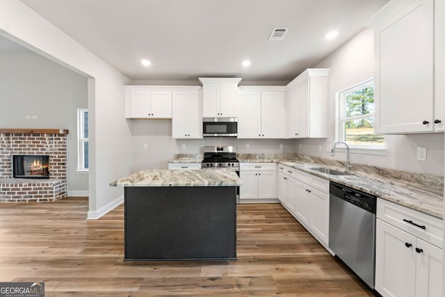 kitchen featuring white cabinets, appliances with stainless steel finishes, a kitchen island, a fireplace, and sink