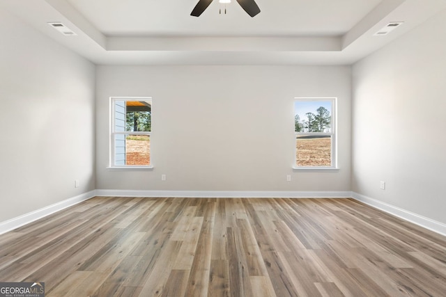 spare room featuring a raised ceiling, ceiling fan, and light hardwood / wood-style flooring