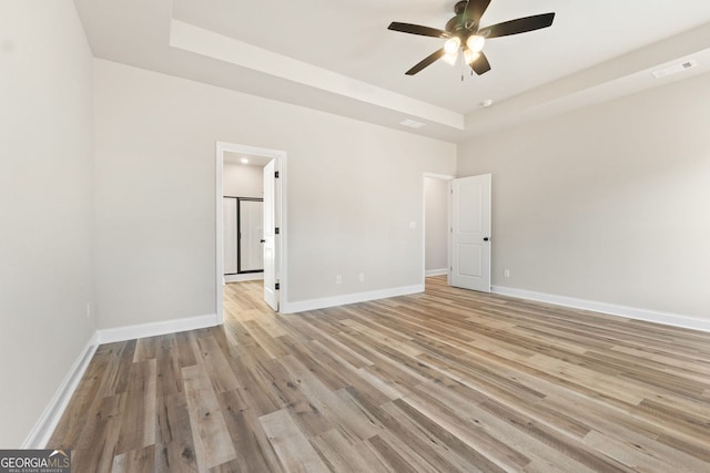 spare room with ceiling fan, a tray ceiling, and light hardwood / wood-style floors