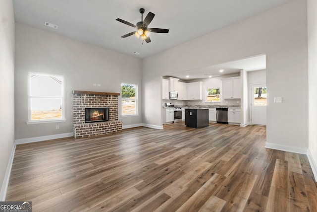 unfurnished living room featuring a brick fireplace, sink, hardwood / wood-style floors, and ceiling fan