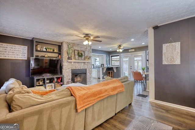 living room featuring a textured ceiling, french doors, ceiling fan, wood-type flooring, and a stone fireplace