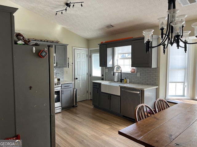 kitchen featuring lofted ceiling, light hardwood / wood-style flooring, a wealth of natural light, gray cabinets, and appliances with stainless steel finishes