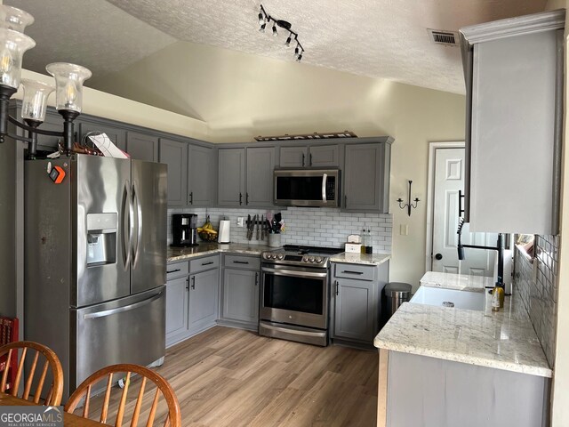 kitchen featuring vaulted ceiling, light hardwood / wood-style floors, backsplash, gray cabinets, and appliances with stainless steel finishes