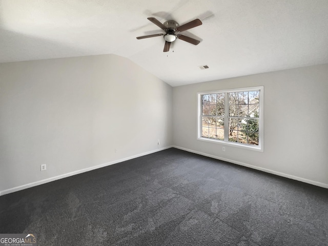 spare room with ceiling fan, vaulted ceiling, and dark colored carpet