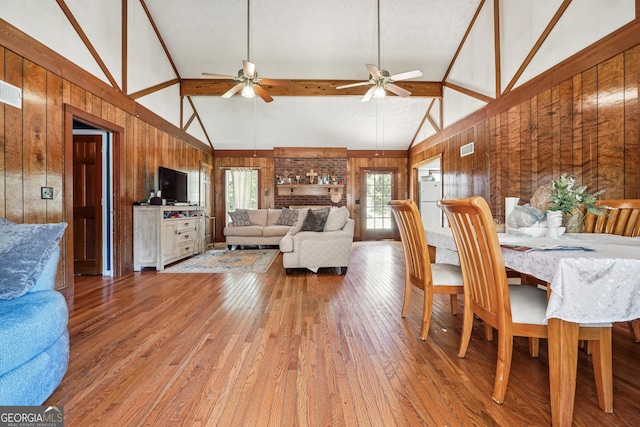 dining area with wood walls, lofted ceiling with beams, and ceiling fan