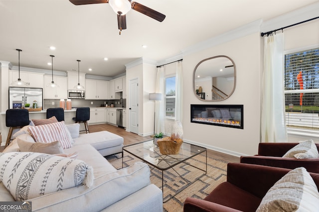 living room with a large fireplace, ceiling fan, light wood-type flooring, and crown molding