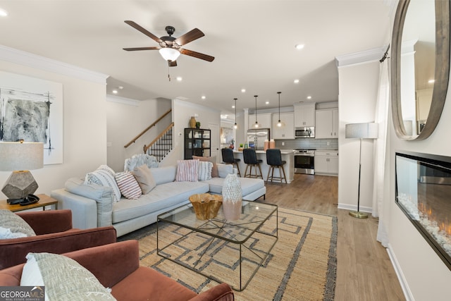 living room with ceiling fan, ornamental molding, and light hardwood / wood-style floors