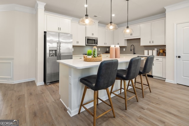 kitchen with stainless steel appliances, white cabinetry, light hardwood / wood-style floors, and an island with sink