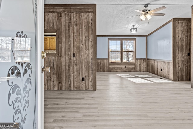 interior space featuring a textured ceiling, ceiling fan, light hardwood / wood-style flooring, and crown molding