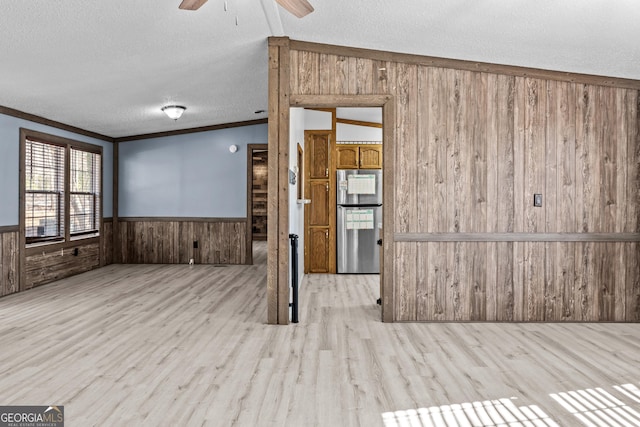 empty room with light wood-type flooring, ceiling fan, ornamental molding, and a textured ceiling