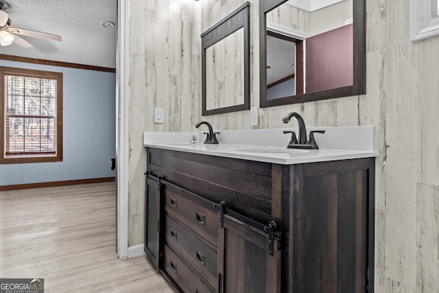 bathroom with wood-type flooring, vanity, ceiling fan, ornamental molding, and a textured ceiling