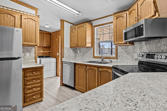 kitchen with appliances with stainless steel finishes, washer and clothes dryer, crown molding, sink, and light hardwood / wood-style flooring