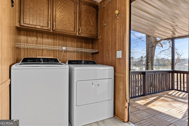 clothes washing area featuring wooden walls, washer and clothes dryer, and cabinets